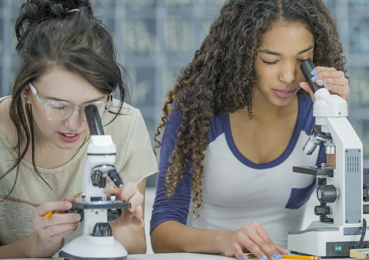 A multi-ethnic group of high school students are working in a science class together. They are looking at slides in biology class through a microscope.