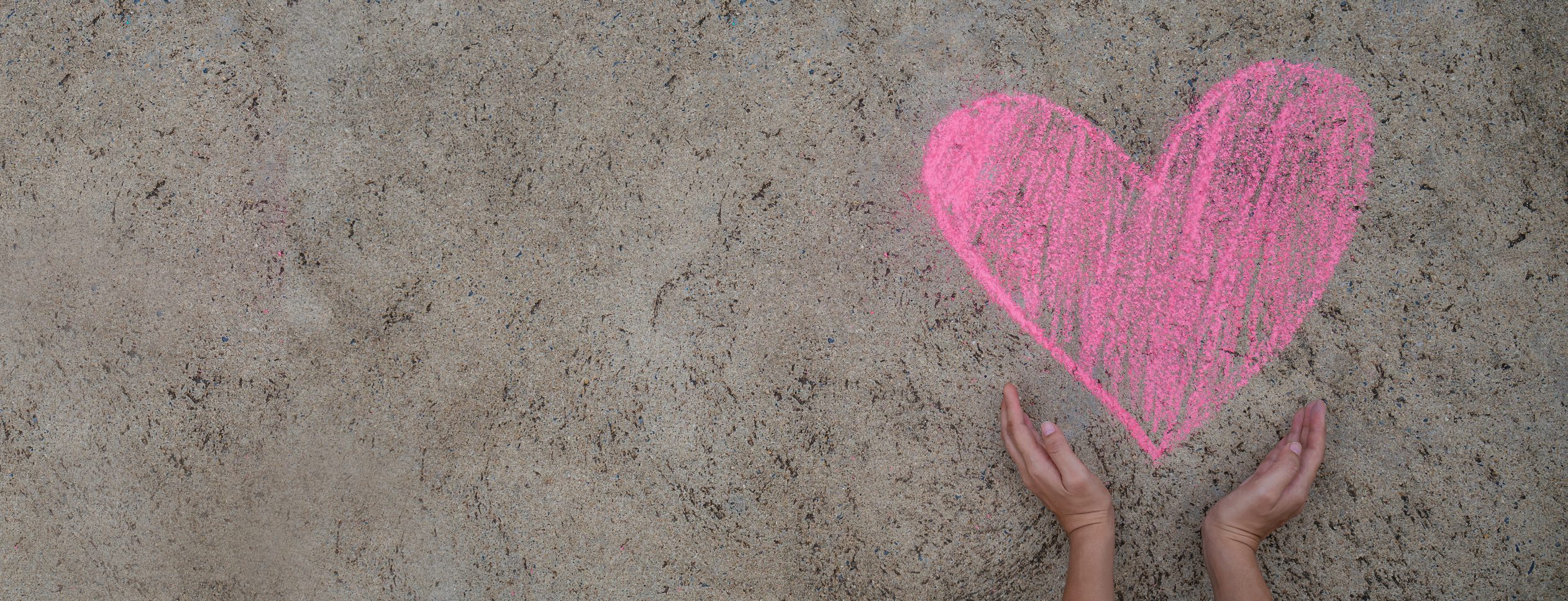 Banner of pink heart drawing with chalk on street floor with two children hands holding